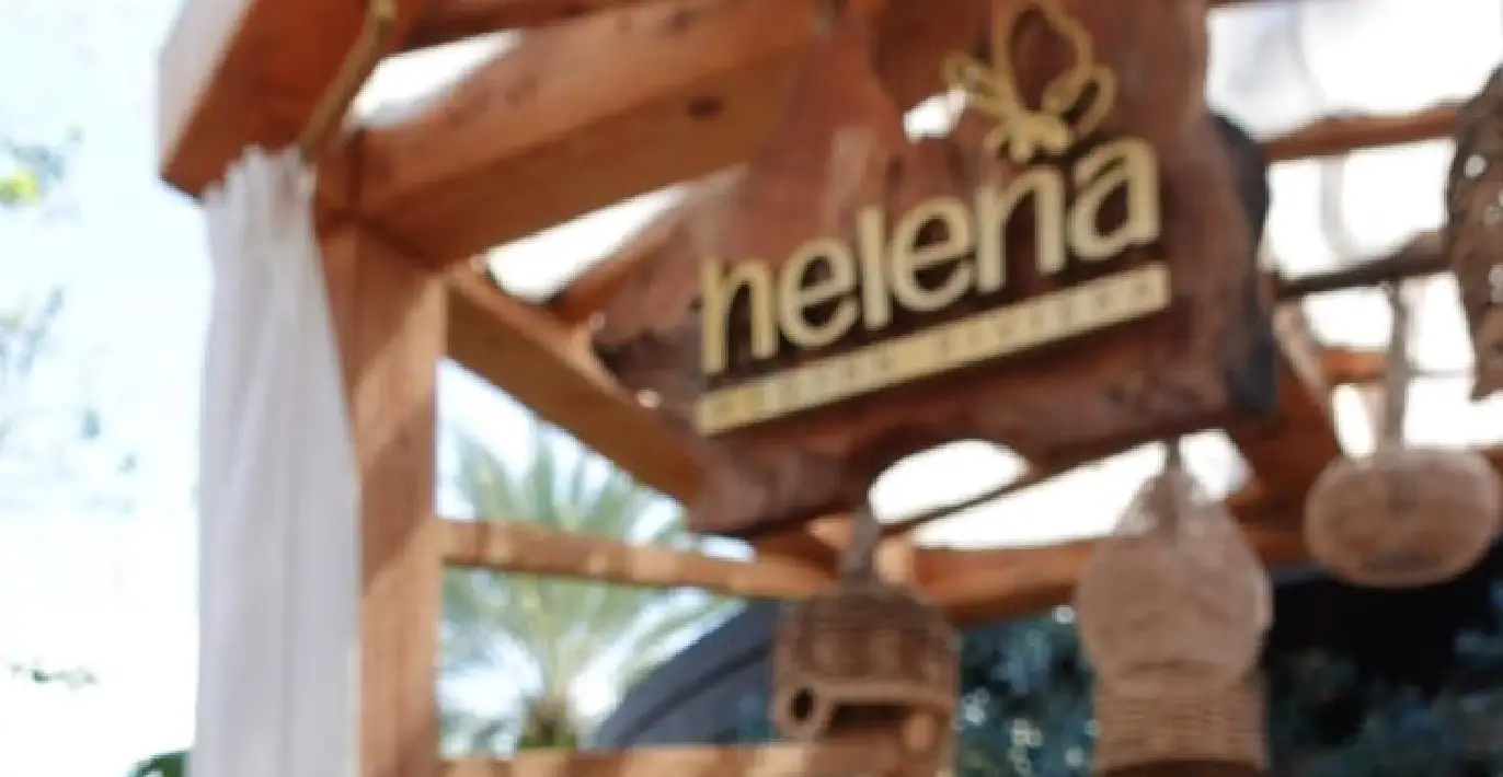 Wooden exterior sign of Helena Organic Bakery, featuring rustic décor with wicker lanterns and natural wood framing under a sunny sky.