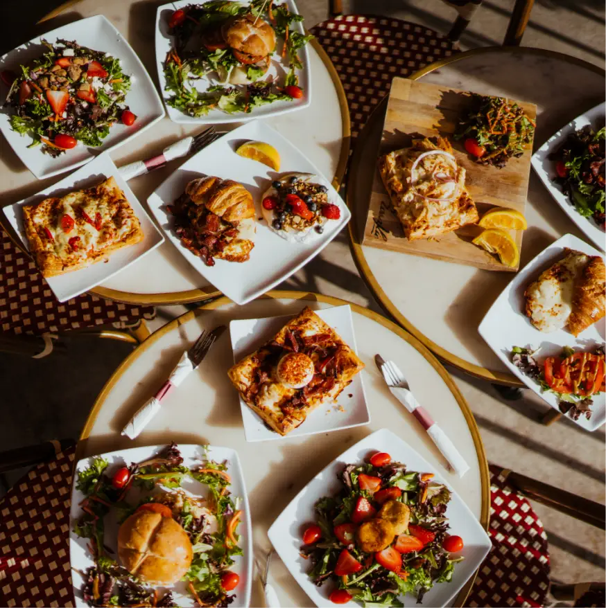 Assorted Rosallie café brunch dishes including fresh salads with strawberries, savory croissants, pastries, and open-faced tarts beautifully arranged on café tables.