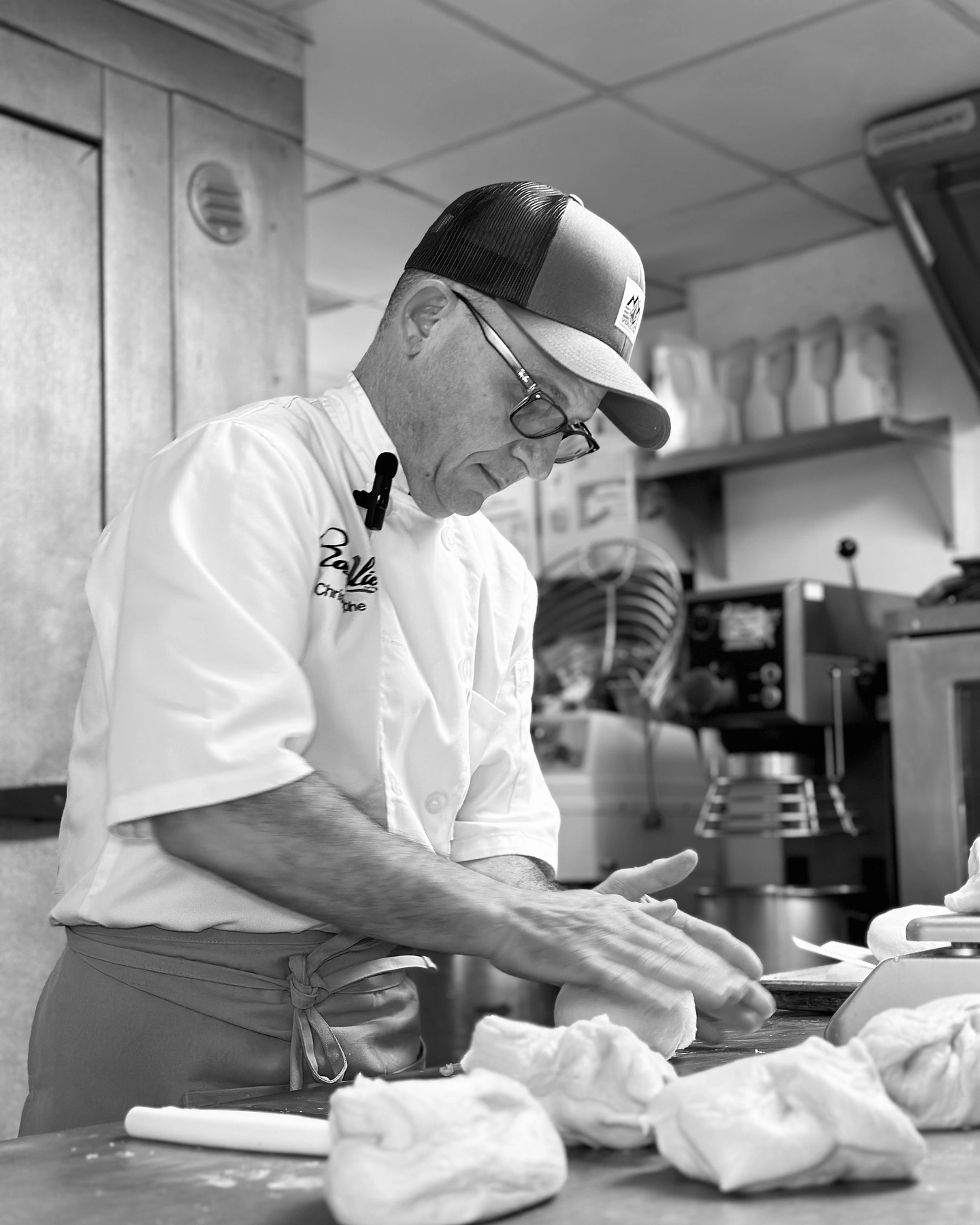 Rosallie café chef preparing fresh pastry dough in the kitchen, wearing a branded uniform and hat, showcasing artisanal baking craftsmanship.